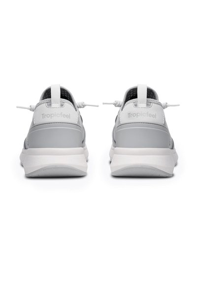Le scarpe Tropicfeel grigie presentano una tomaia in materiale sintetico liscio, un colletto imbottito, lacci elastici e una suola in gomma bianca con un lieve arco.