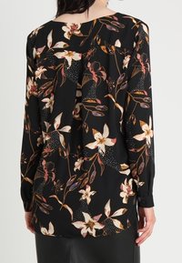 Long-sleeve blouse in black fabric, featuring a floral pattern in cream, pink, and orange. Includes a pleated back and buttoned cuffs.