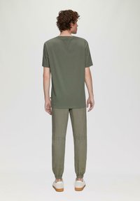 Ciemnozielona krótki rękaw t-shirt z okrągłym dekoltem, zestawiony z jasnoszarymi spodniami typu tapered z elastycznymi mankietami i gładką fakturą, noszony w połączeniu z trampkami.