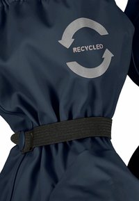 Újrahasznosított sötét tengerészkék dzseki sima textúrával, fekete elasztikus övvel és szürke kör alakú logóval, amely nyilakat és a "RECYCLED" szót tartalmazza.