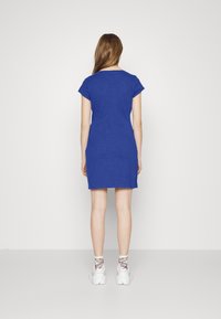 Modrá krátká šaty s krátkým rukávem, do kolen, s přiléhavým střihem, vyrobené z měkkého materiálu s hladkou texturou. Nosené s bílými teniskami.