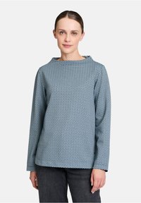 Bluse mit blauen Mustern, rundem Halsausschnitt, langen Ärmeln und einem strukturierten Stoff mit diamantähnlichem Design.