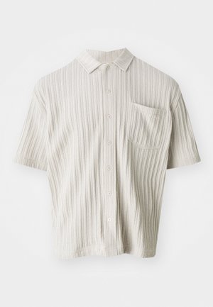 Kortermet, lys beige skjorte med krage, vertikal ribbet tekstur, fem knapper og en brystlomme.