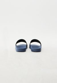 Blå gummisandaler med teksturert såle. Åpent design med to svarte stropper plassert over foten. Flat, slank form.