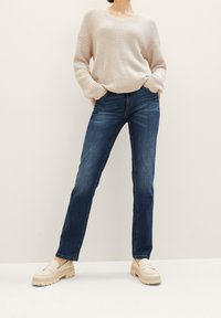 Beige stickad tröja med V-ringning, ihopparad med blå raka jeans. Skorna är ljusa plattformsskor.