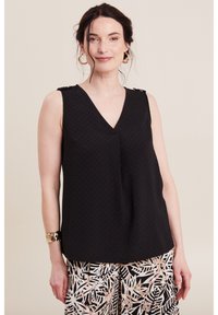 Top nero senza maniche con scollatura a V, caratterizzato da un tessuto testurizzato e dettagli decorativi sulle spalle. Abbinato a pantaloni con fantasia.