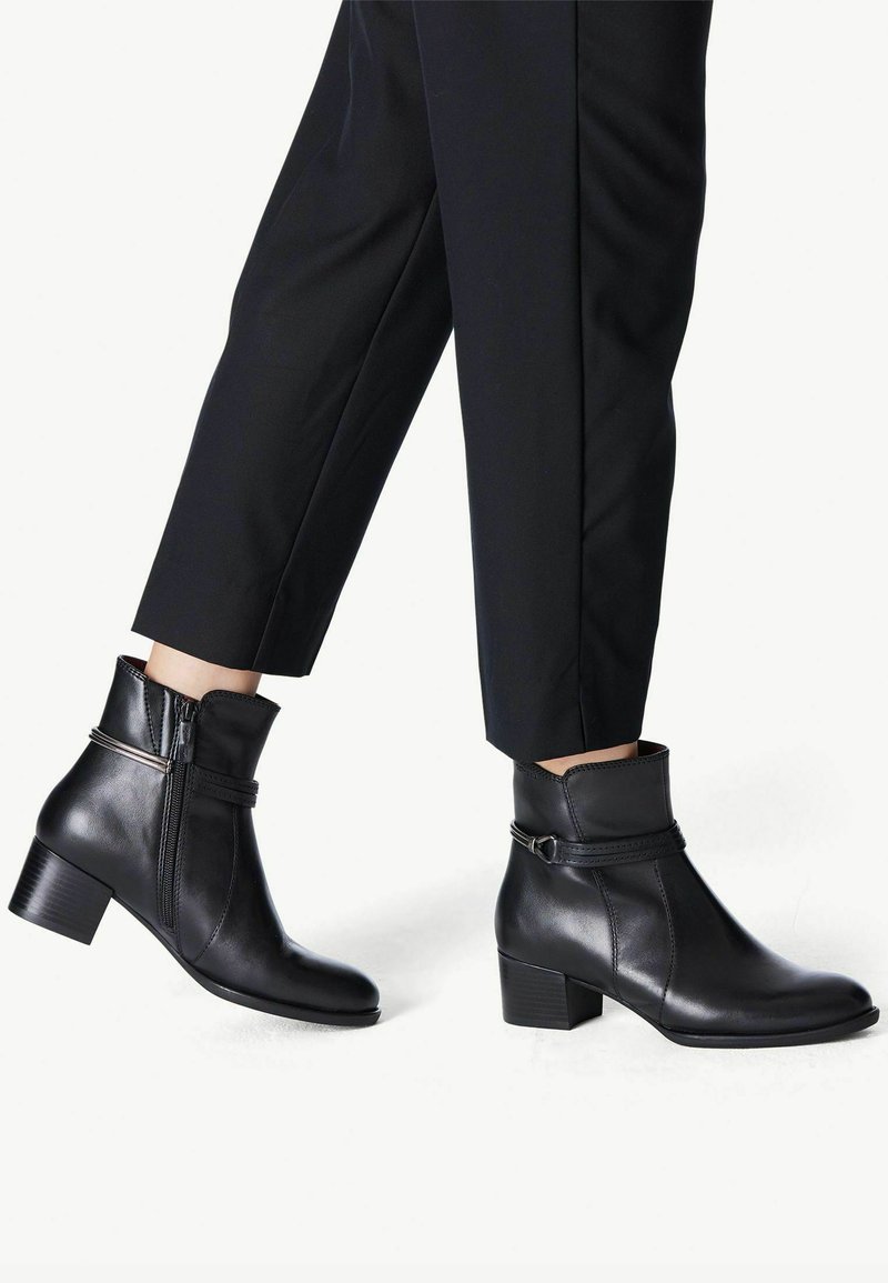 Bottines en cuir noir avec une fermeture éclair sur le côté, un tige effilée et un talon bloc, comportant un accent de sangle décoratif près du haut.