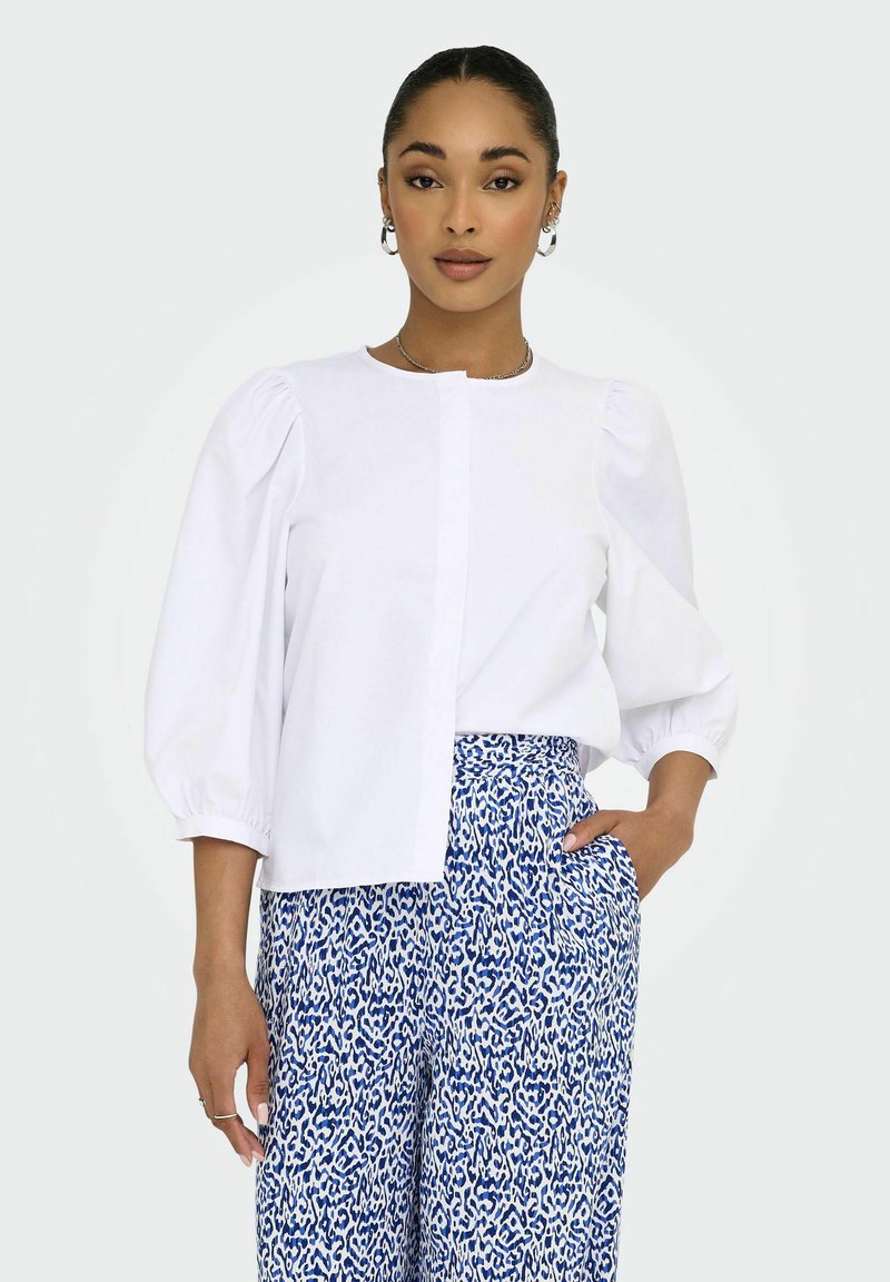 Witte blouse met pofmouwen en een rechte snit, gecombineerd met blauwe wijdvallende broek met een abstracte print.