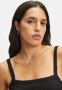 Zilveren ketting en bijpassende oorbellen met rechthoekige vormen; gladde afwerking; gedragen met een zwarte geribbelde tanktop.