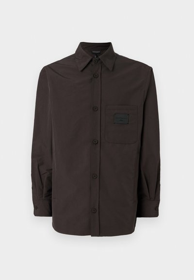Πουκάμισο με κουμπιά σε σκούρο καφέ χρώμα, με κοφτό κολάρο, μακριά μανίκια, μία τσέπη στο στήθος και υφή υφάσματος.