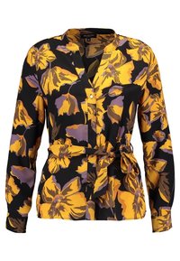 Långärmad svart blus med mönster av gula och lila blommor, knäppning framtill, utan krage och med band i midjan för extra form.