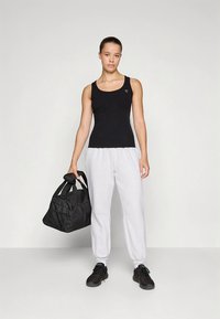 Must tankitopp hallide dressipükstega, millel on elastne vöökoht, mida hoiab must spordikott, kantud tumedate jalanõudega.