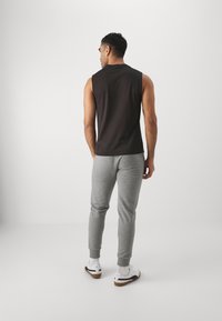 Zwart mouwloos shirt gecombineerd met grijze sweatpants, met taps toelopende broekspijpen en ribgebreide boorden. Witte sneakers met zwarte accenten.
