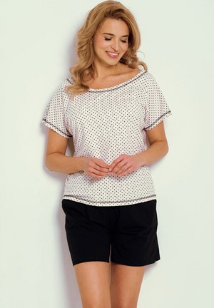 Jasnoróżowa bluzka w groszki z szerokim dekoltem i krótkimi rękawami, zestawiona z czarnymi szortami. Ozdobiona dekoracyjną lamówką na krawędziach.