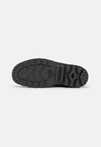 Semelle de chaussure en caoutchouc noir avec des motifs de garniture texturée, des rainures et des bords arrondis. Comprend de petits trous pour le drainage et un détail de logo.