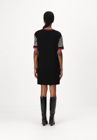 Schwarzes Kleid mit kurzen Ärmeln im Leopardenmuster und rosa gestreiften Akzenten. Das Model trägt schwarze knielange Stiefel mit Absatz. Einfarbiger Hintergrund.