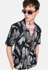Camisa de manga corta con fondo negro y patrones de olas blancas en contraste. Fabricada con tela ligera, tiene un corte holgado y cuello.