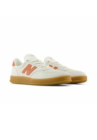Zapatillas de ante blancas con acentos naranjas y suela de goma. Presentan detalles perforados y un diseño cosido. Ligeras y de corte bajo.
