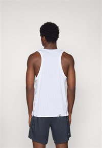 White sleeveless athletic tank top with side slits, paired with dark gray shorts, featuring a subtle logo detail near the hem.
