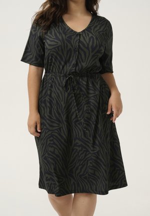 Woman wearing knee-length, short-sleeve dress with black and dark green zebra print, buttoned front, and a tied waist belt.
