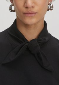 Zwarte top met een grote geknoopt kraag, gemaakt van zacht materiaal. Het ontwerp heeft een gladde textuur en een minimalistische stijl.