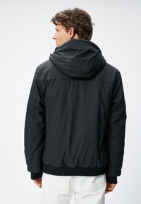 Zwarte gewatteerde jas met een capuchon, elastische manchetten en zoom. Gladde textuur zonder zichtbare patronen of hardwaredetails. Minimalistisch ontwerp.