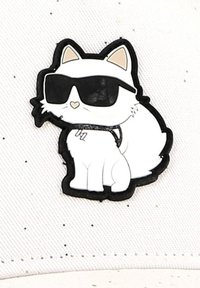 Witte kattencartoon pin met een zwart montuur, die zwarte zonnebrillen draagt, omrand met zwart, met een eenvoudig ontwerp op een gestructureerde witte achtergrond met spikkels.