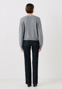 Maglione grigio a maglia con una vestibilità relaxed e maniche lunghe, abbinato a jeans denim scuri con gamba dritta e dettagli di cucitura discreti.