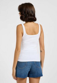 Weißes, geripptes Tanktop mit quadratischem Ausschnitt, kombiniert mit blauen Jeansshorts mit fransigen Säumen und Gesäßtaschen.