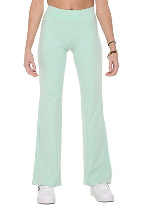 Modèle portant un pantalon évasé taille haute vert menthe et des baskets blanches sur un fond blanc uni.
