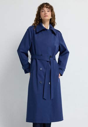 Marineblå trenchcoat med dobbeltradet design, stor krave, talje med bælte og sidelommer. Lavet af glat stof med mat finish.