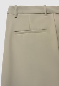 Beige Hosen mit glatter Textur, flachem Taillenbund und einer einzelnen Gesäßtasche. Dezente Nahtdetails ergänzen das Design.