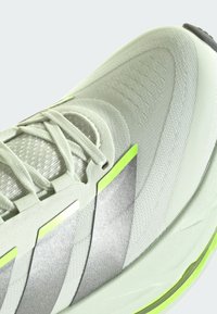 Chaussure de sport gris clair avec des bandes argentées réfléchissantes, des accents vert clair, une tige en maille et des lacets blancs vue de dessus.
