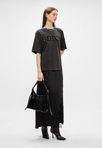 Μαύρη βαμβακερή μπλούζα με γραφικό "ΕΛΕΥΘΕΡΙΑ", συνδυασμένη με μια μακριά μαύρη φούστα. Αξεσουάρ περιλαμβάνουν μια μαύρη δερμάτινη τσάντα και μυτερές μαύρες μπότες.