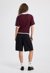 Short-sleeve, maroon knit sweater with light blue and white accents, paired with black tailored shorts. Textured fabric, relaxed fit.