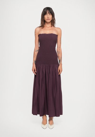 Robe violette sans bretelles avec un corsage texturé et une jupe plissée fluide. Tissu lisse avec un détail de col froncé. Chaussures non détaillées.