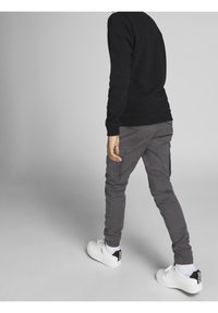 Svart sweatshirt och grå cargo-byxor med sidofickor, ihop med vita sneakers med svarta accenter på hälen.