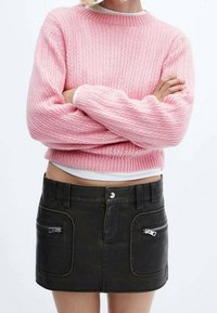 Rosa, kurz geschnittenes Strickoberteil mit gerippter Textur, kombiniert mit einem dunkelgrünen, denimini Minirock mit zwei Reißverschlusstaschen.