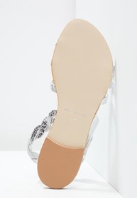 Harmaa avonainen sandaali, jossa on punotut hihnat, sileä sisusta, kiinteä vaaleanruskea pohja ja kohokuvioitu "Made in Italy" sekä koon 37 merkinnät.