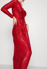 Rotes, mit Pailletten besetztes Abendkleid mit langen Ärmeln, V-Ausschnitt und verdrehtem Taillendesign. Das Material ist glatt und glänzend und reflektiert das Licht.