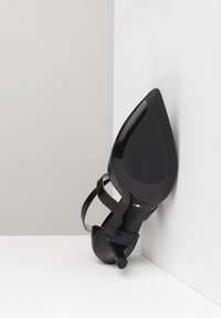 Chaussure à talon haut noire avec un bout pointu et des sangles en cuir fines. Marquée "Fabriqué en Italie" et taille 37. Texture lisse et design épuré.