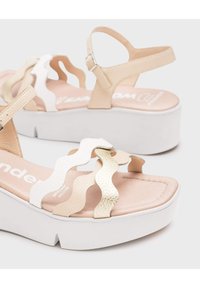 Sandalias de plataforma con un diseño ondulado en blanco y beige, con tiras texturizadas y una plantilla beige suave sobre una suela blanca.
