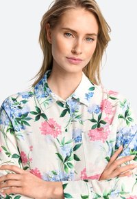 Bloemige knoopsluiting overhemd van lichtgewicht stof met roze en blauwe bloemen op een witte achtergrond. Inclusief een zak en een kraag.