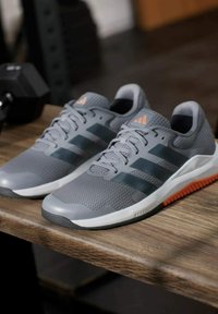 Zapatillas deportivas grises con parte superior de malla, rayas negras, detalles en naranja y suelas de goma. Diseño texturizado con cierre de cordones.