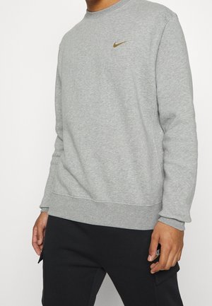Grå sweatshirt lavet af blødt stof, med rund halsudskæring og ribbede manchetter, med et lille gyldent Nike-logo på brystet.
