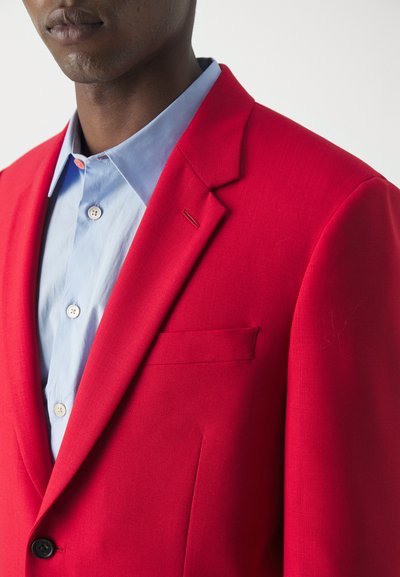 Rød skræddersyet blazer med notklap, enkelt lomme og letvægtsstof. Lyseblå skjorte med krave nedenunder har runde knapper.
