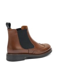 Bota Chelsea de cuero marrón con paneles elásticos negros a los lados, detalles de picado en la punta y una suela negra gruesa.