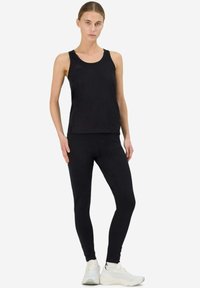 Canottiera sportiva nera e leggings, realizzati in un materiale liscio ed elastico. Presentano una leggera lucentezza e un branding minimale. Sono completati da sneakers bianche.