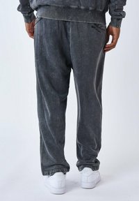 Joggers grises de corte relajado en un tejido cepillado con una textura deslavada; cuenta con bolsillos laterales y una cinturilla elástica. Zapatillas blancas visibles.