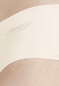 Cremfarbene Sloggi-Unterwäsche aus glattem, elastischem Stoff. Verfügt über einen breiten Bund mit dezent eingeprägtem Markenlogo.